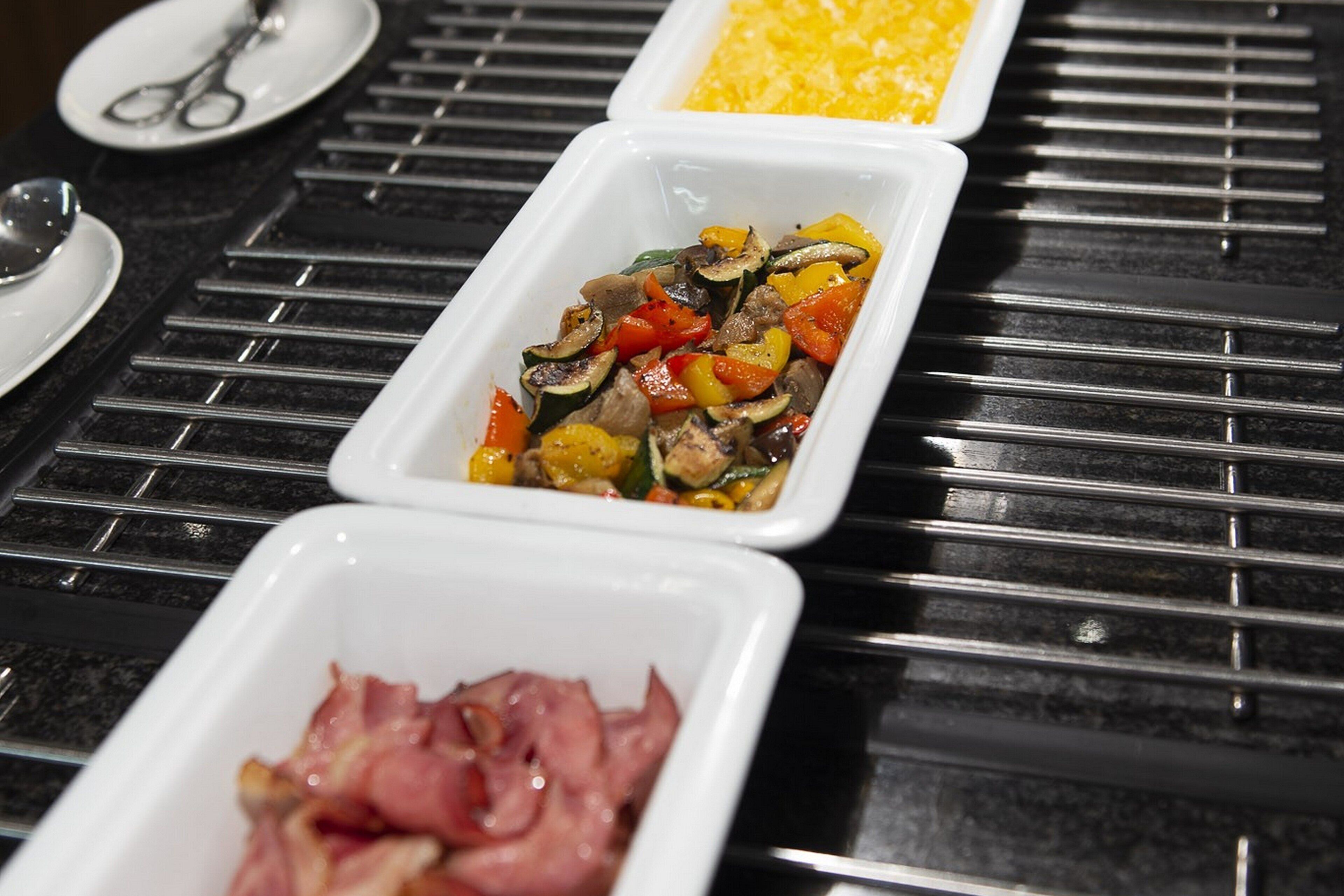 Una mesa de buffet con tres opciones: verduras a la parrilla, huevos revueltos y tocino.