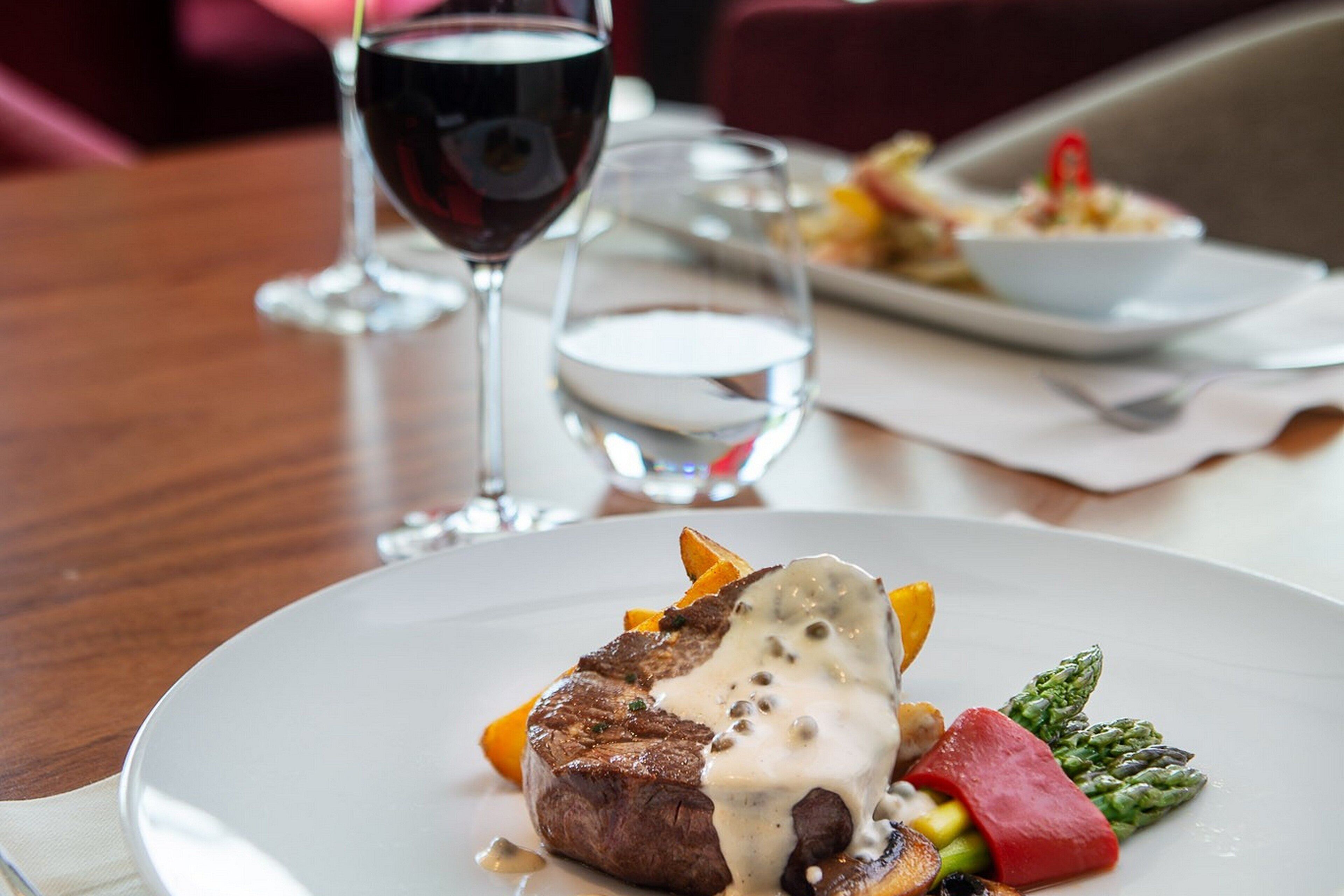 A dining table with a plate of food, a glass of red wine, and a glass of water.