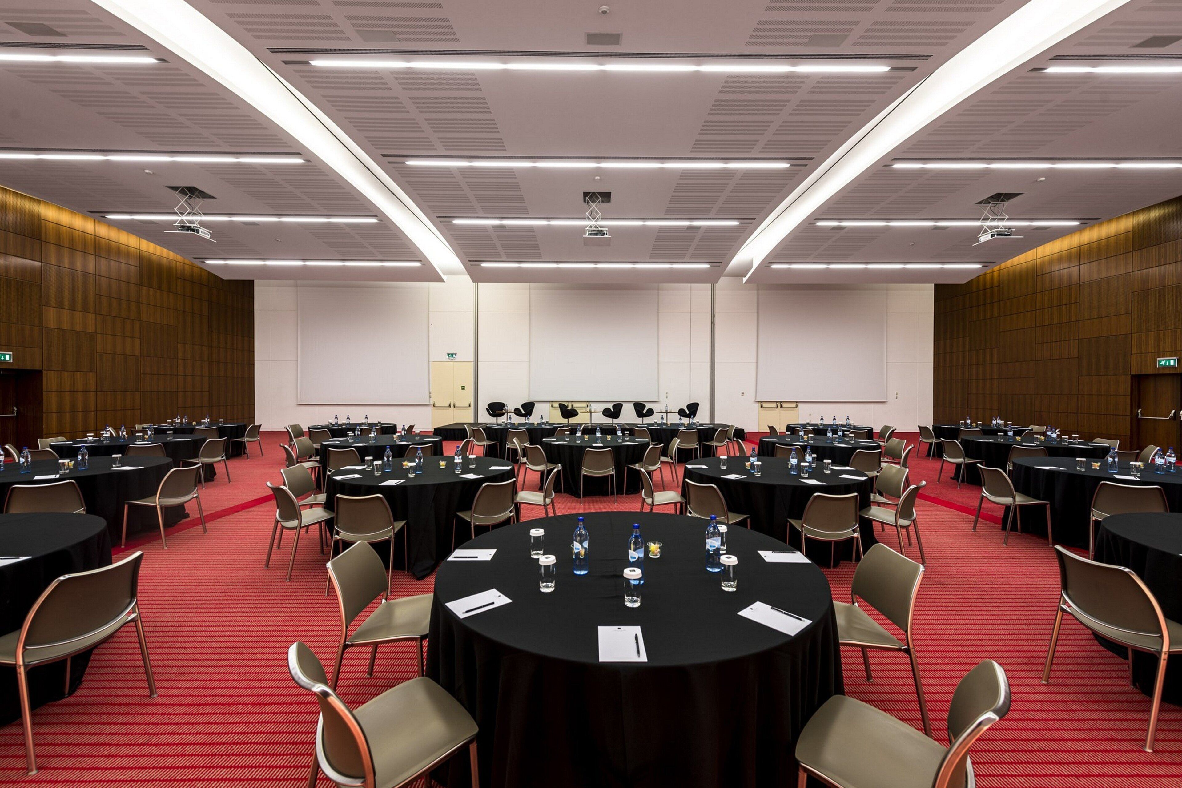 Une salle de conférence équipée de tables rondes, de chaises et d’une scène.
