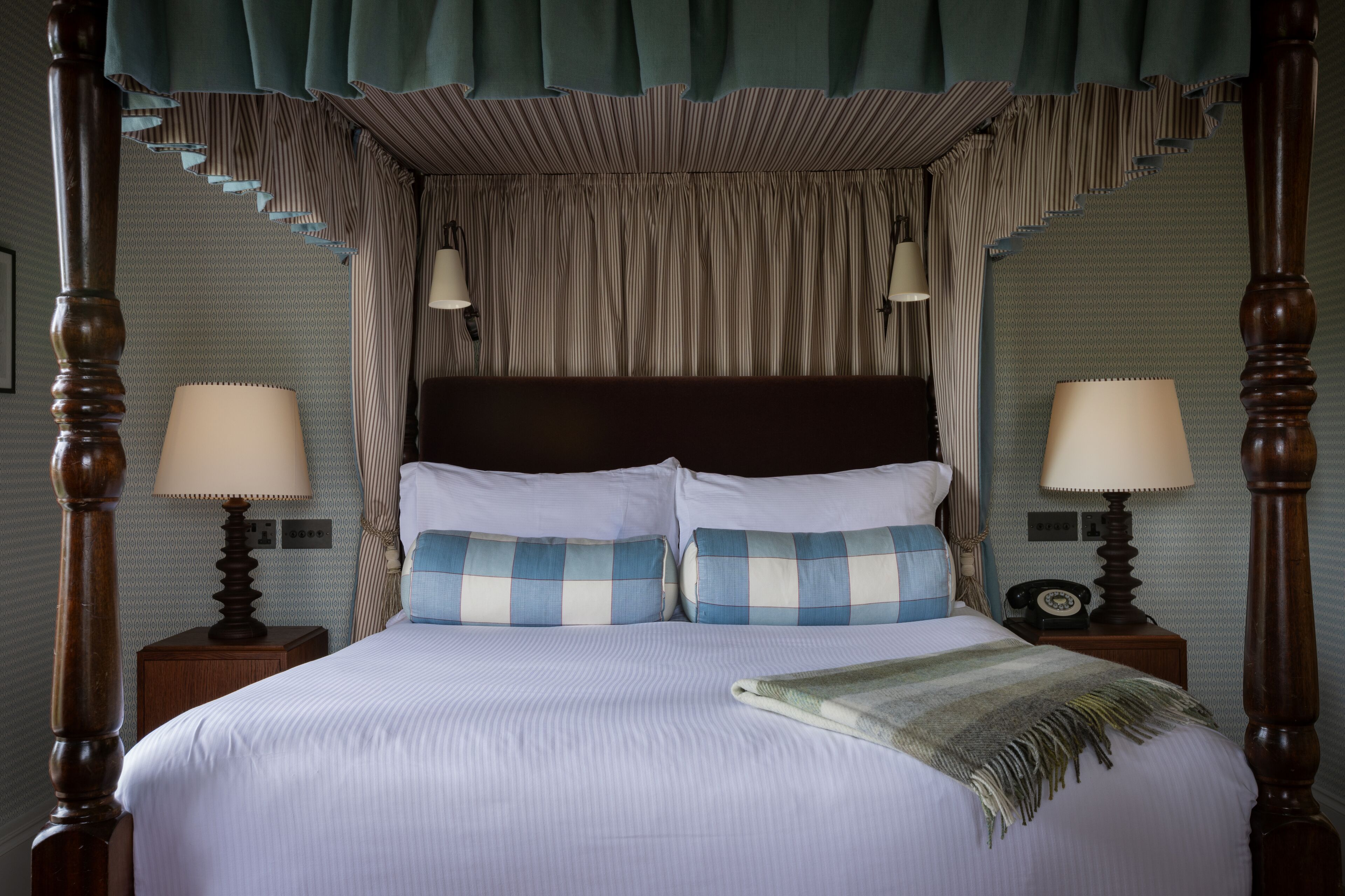 A four-poster canopy bed with two bedside tables, each with a lamp and a telephone.