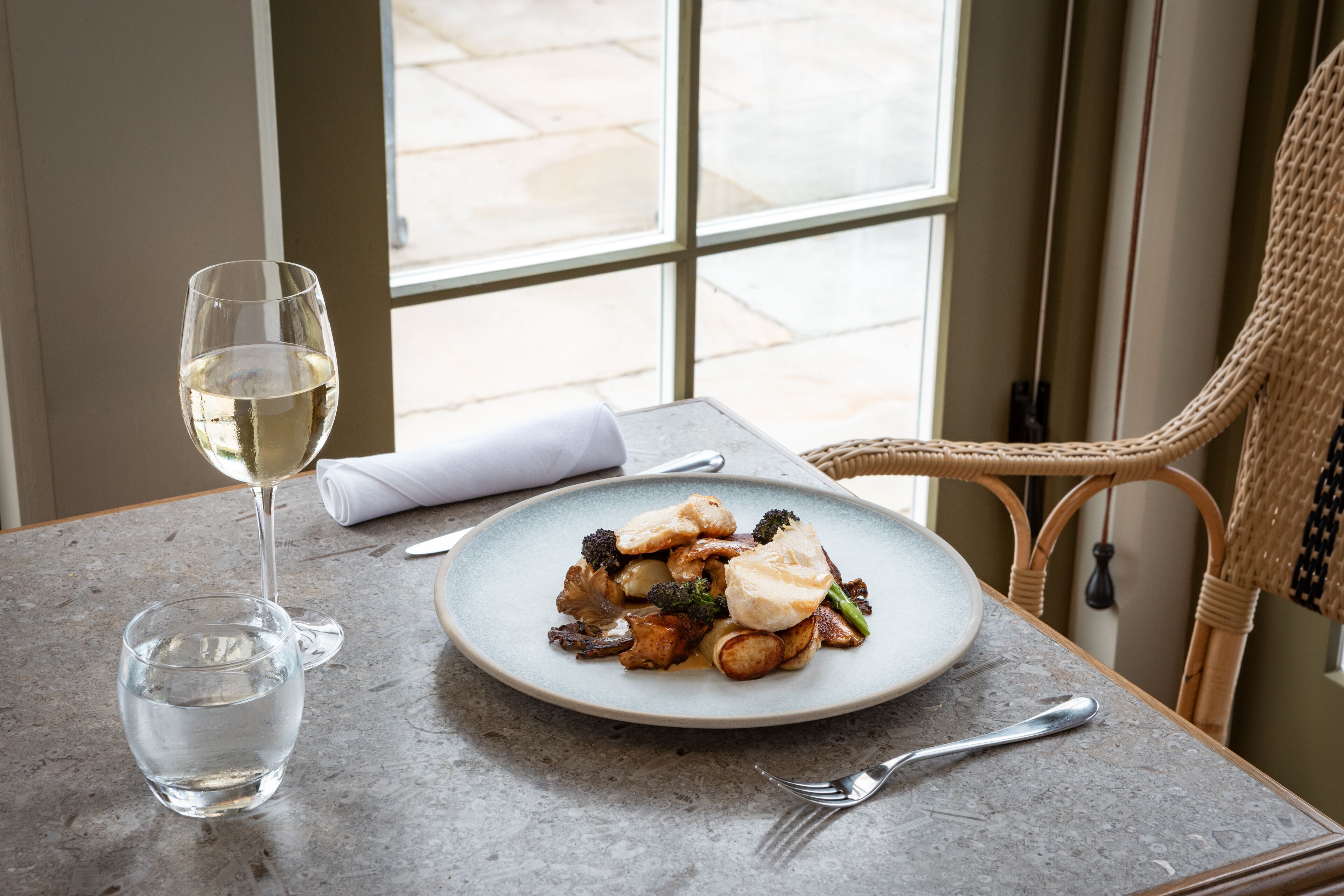 A dining table with a plate of food, a glass of water, and a wine glass.
