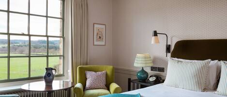 A hotel room with a large window, a bed, a chair, a table, and a lamp.