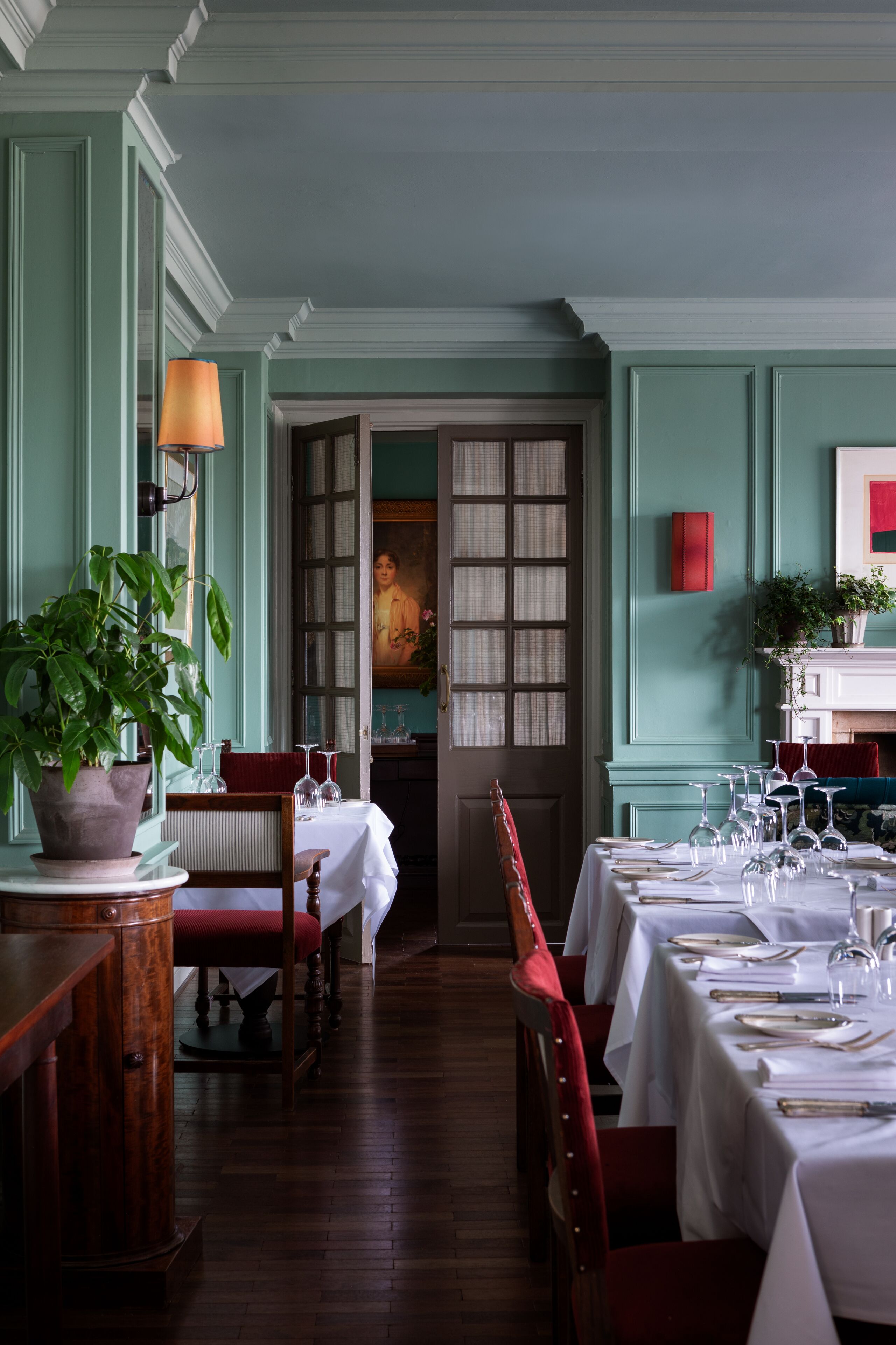 A dining area with tables set for a meal, chairs, a potted plant, and a lamp.