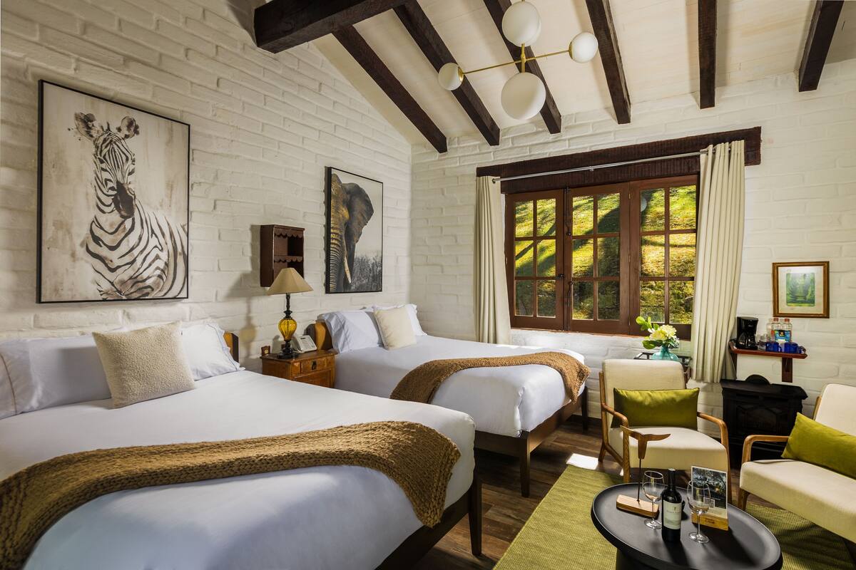 A hotel room with two beds, a sofa, a fireplace, and artwork on the walls.