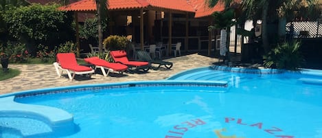Una piscina con sillones de descanso y palmeras.