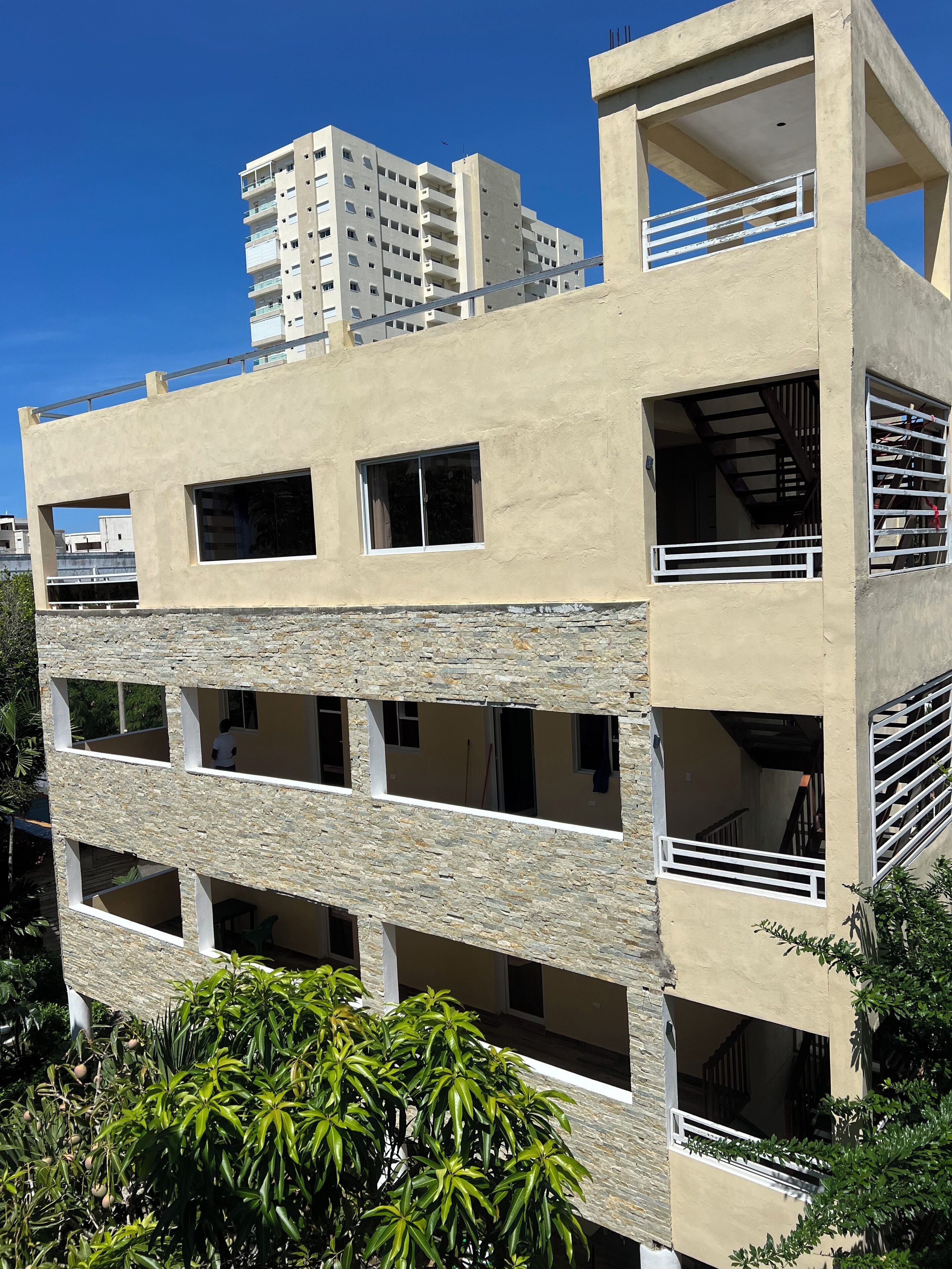 Un edificio de varios pisos con balcones y ventanas amplias, rodeado de vegetación.