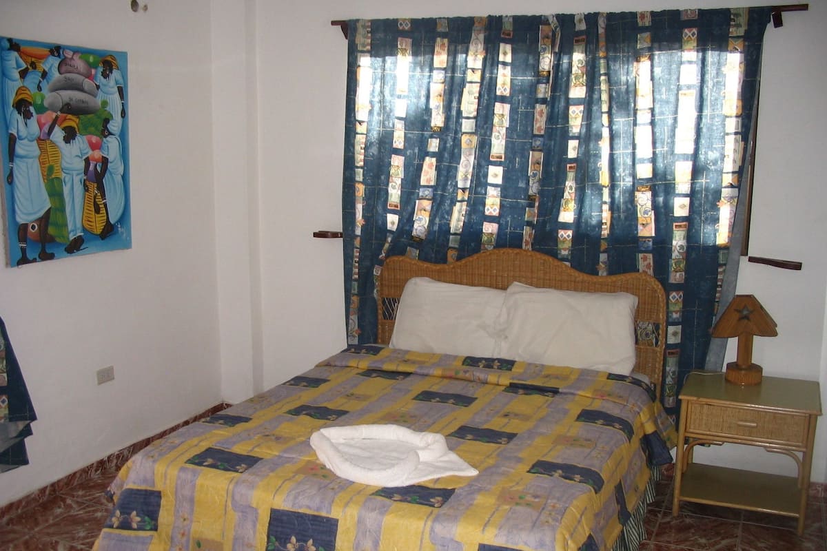 A bedroom with a bed, a nightstand, a lamp, and a painting on the wall.