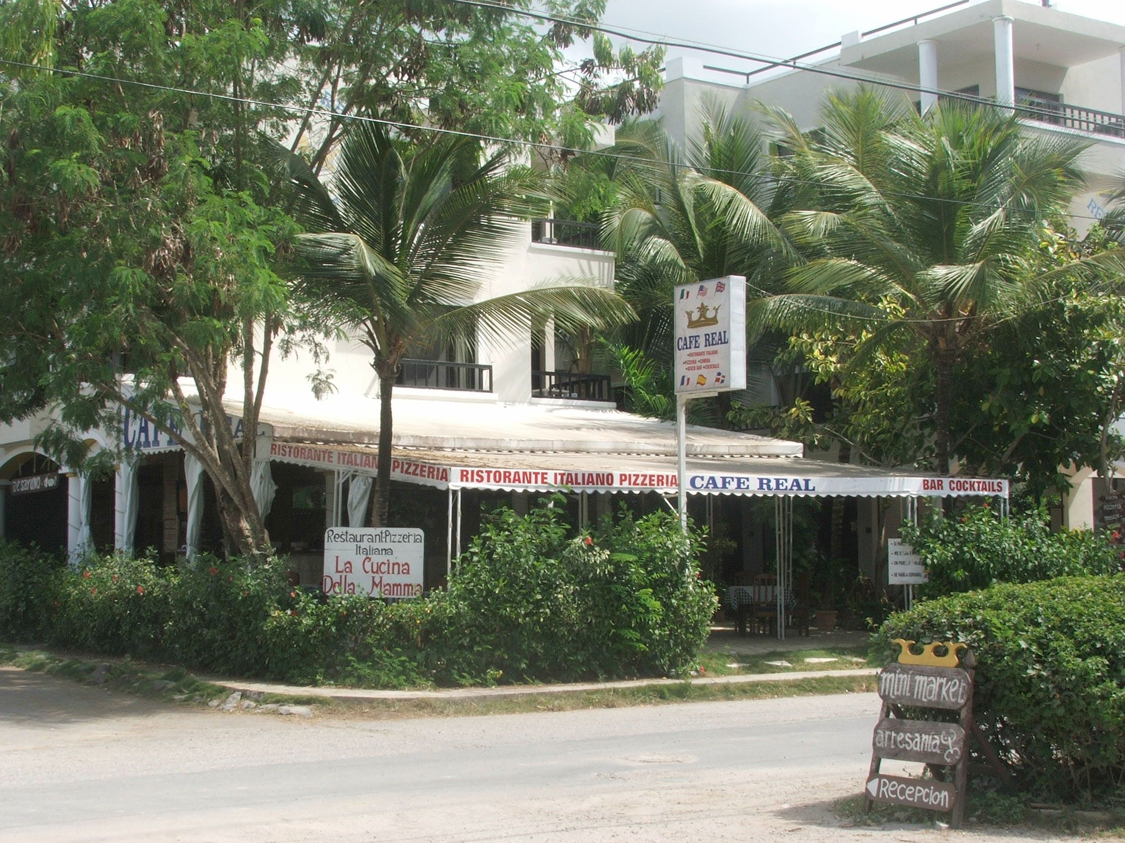 A restaurant with a sign reading "Cafe Real" and "Bar Cocktails" in front of a building with a white facade and a covered patio area.