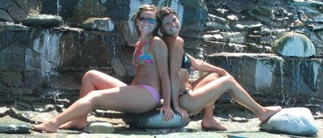 Two people sitting by a pool with a rocky backdrop.