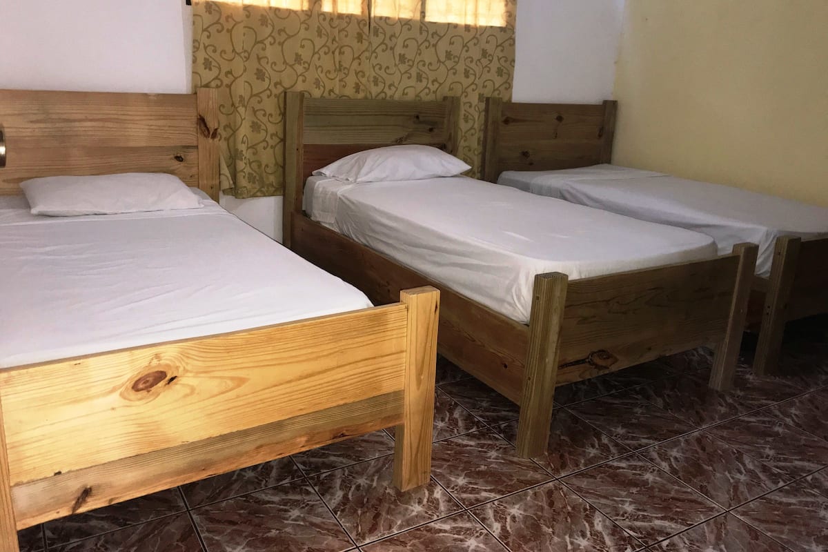 A room with three wooden beds, a wooden nightstand, and a patterned curtain.