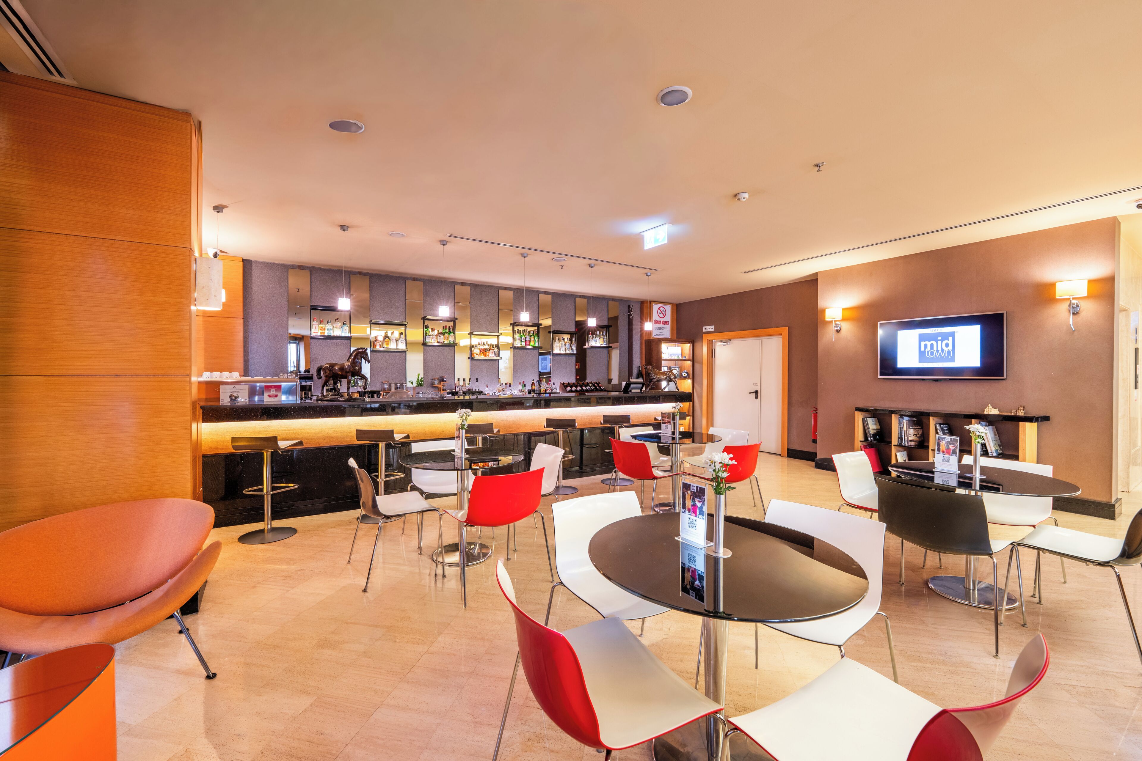 A hotel lobby with a bar area, seating arrangements, and a television screen.