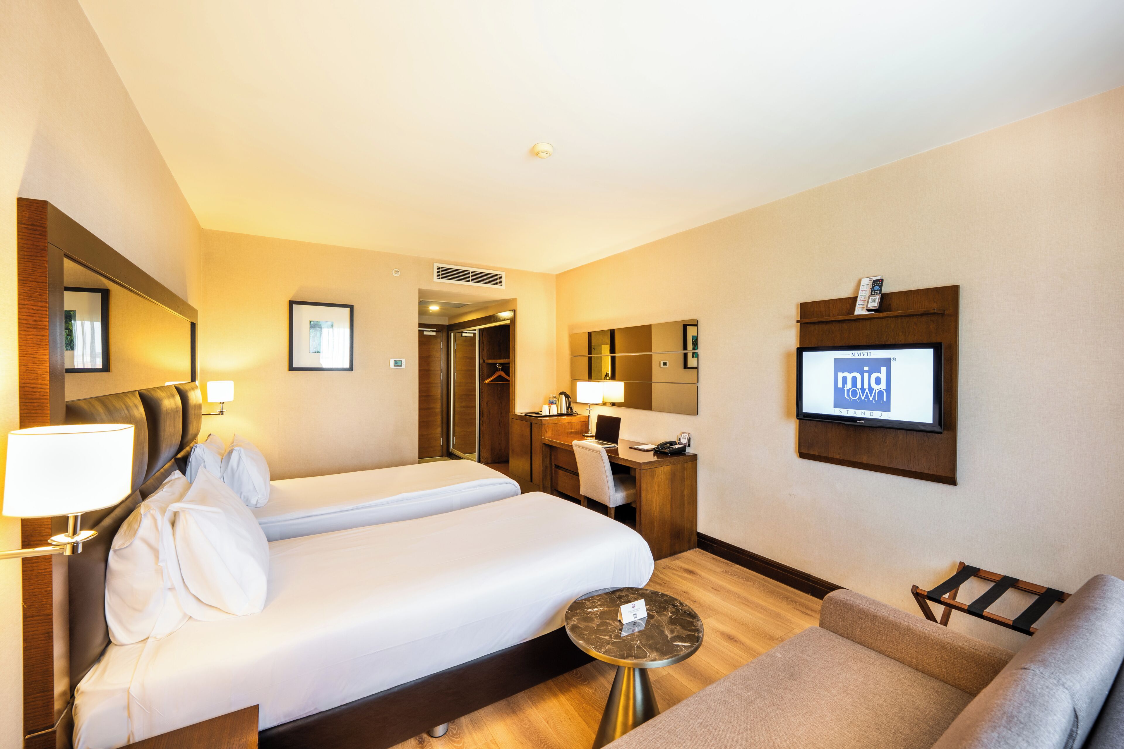 A hotel room with two beds, a desk, a chair, a TV, and a small table.
