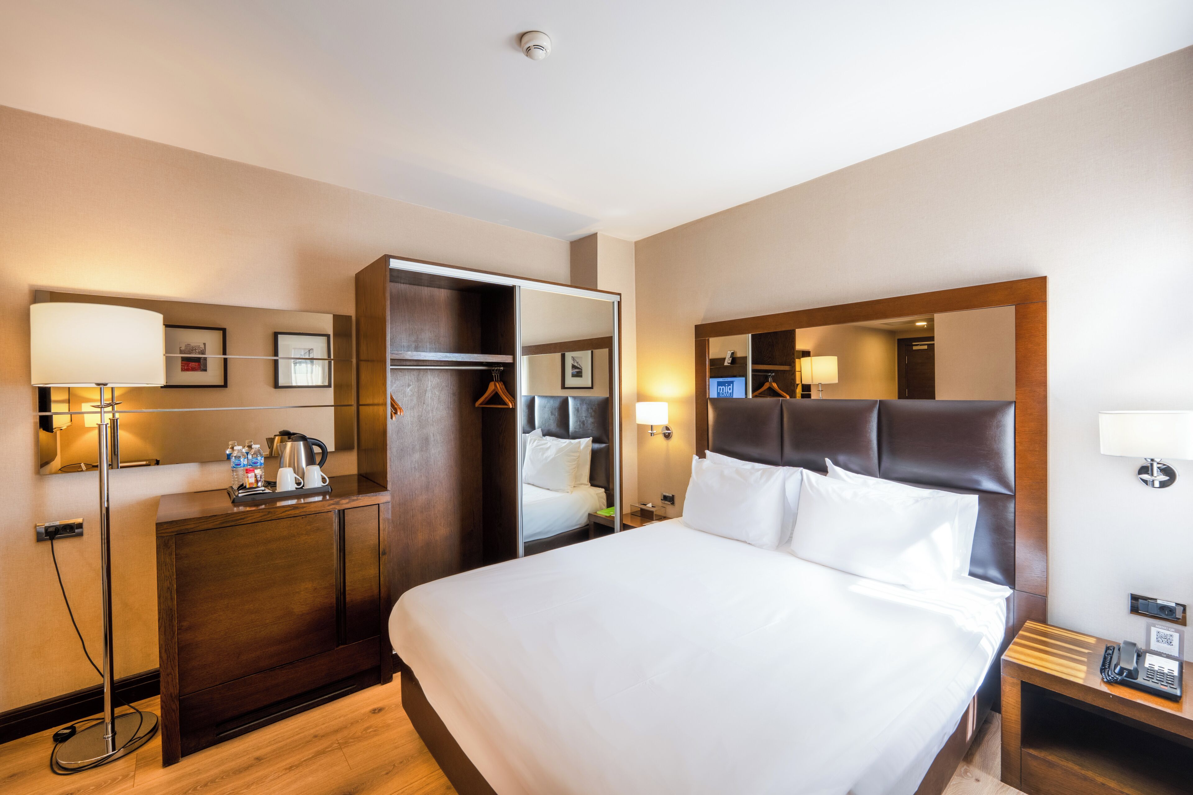 Ein Hotelzimmer mit einem großen Bett, einem Kleiderschrank, einem Schreibtisch und einem Spiegel.