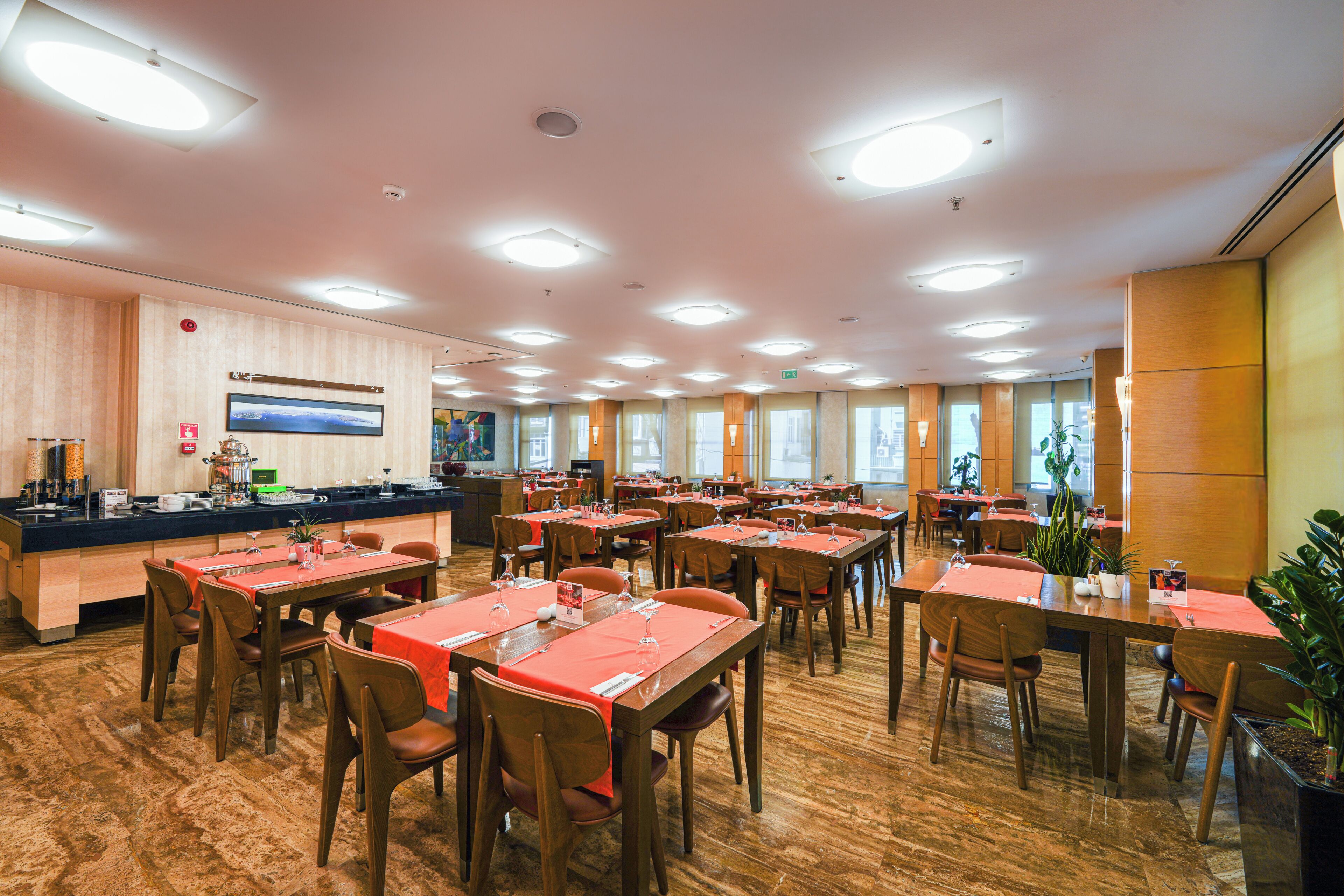 A spacious dining area with multiple tables and chairs, a counter with a display, and large windows allowing natural light.