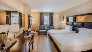 Ένα δωμάτιο ξενοδοχείου με δύο κρεβάτια, ένα γραφείο με έναν φορητό υπολογιστή, μια καρέκλα, μια τηλεόραση και ένα παράθυρο με κουρτίνες.