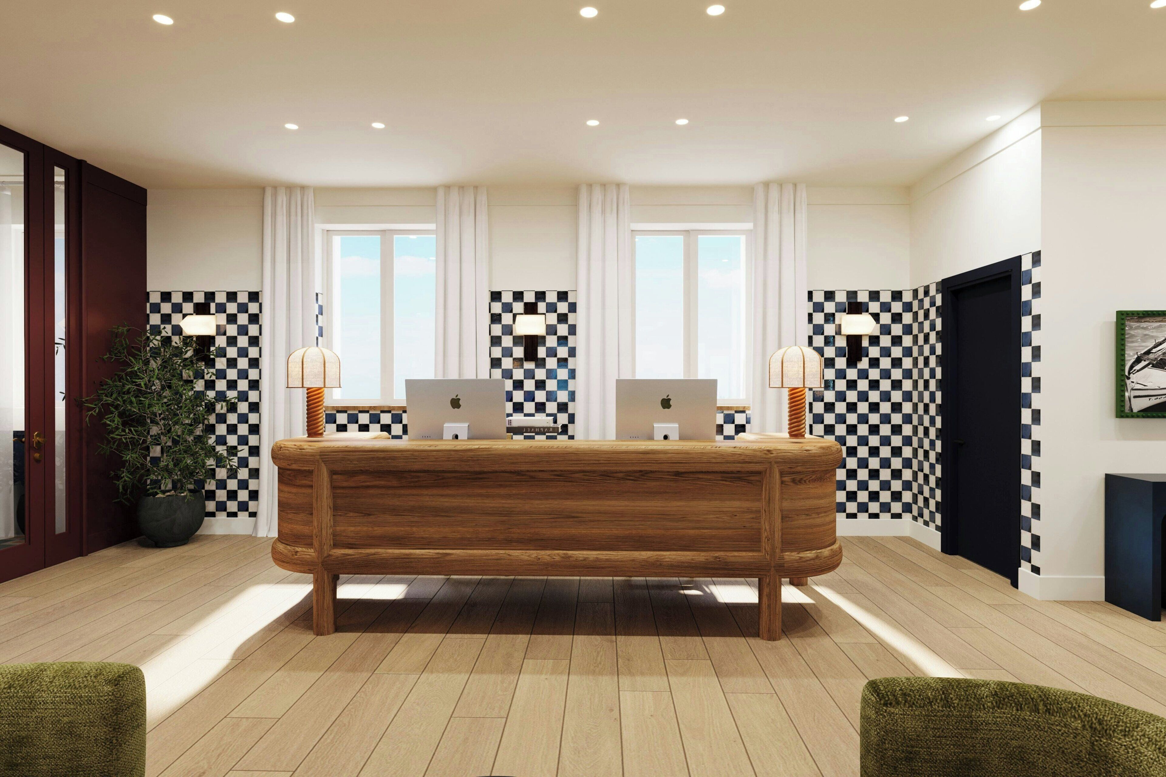 Un mostrador de recepción con dos computadoras, una planta en maceta y azulejos de diseño cuadriculado.