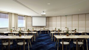A conference room with a large screen, multiple tables, chairs, and a blue carpet.