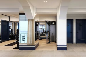 A modern gym with exercise equipment, a staircase, and a view of the sea.