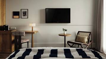 A hotel room with a bed, a desk with a lamp, a chair, a television, and two framed pictures on the wall.