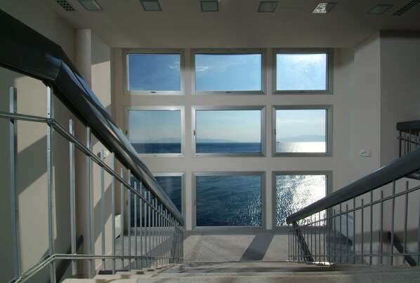 A staircase with metal railings leading to a landing with large windows offering a view of the sea. - Jadran, Rijeka, a Tribute Portfolio Hotel (Rijeka)