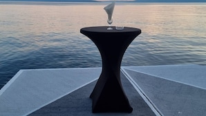 A table with a glass on it, placed on a concrete platform by a body of water.