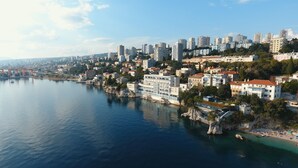 A coastal cityscape with high-rise buildings, a marina, and a rocky shoreline.