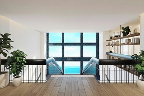 Un intérieur moderne avec vue sur la mer, comprenant un plancher en bois, une rambarde noire et une bibliothèque.