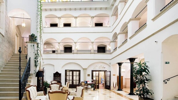 Un atrio de varios niveles con una escalera, zona de estar y un restaurante llamado 'L'Olive'.