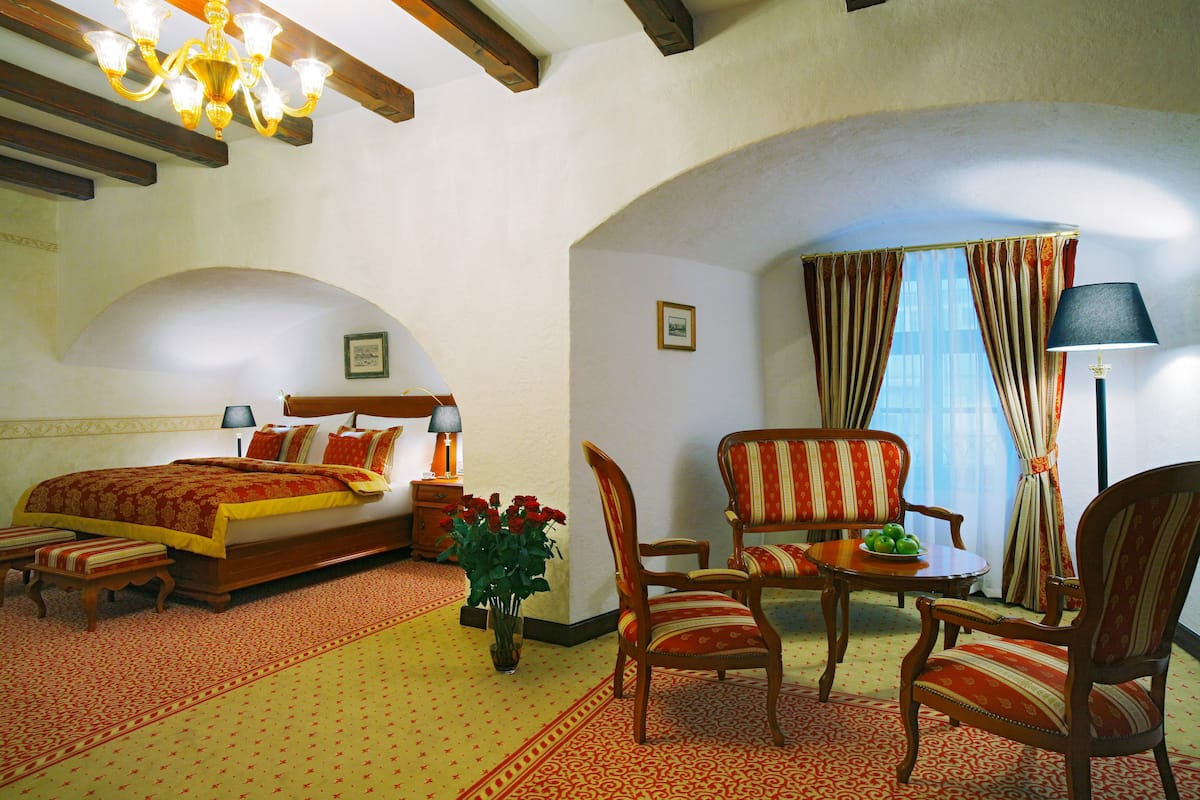Ein Hotelzimmer mit Bett, einer Sitzecke mit Stühlen und Tisch, einer Lampe und einer Vase mit Blumen.