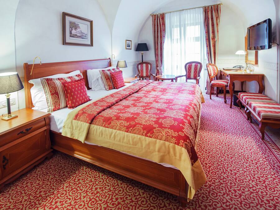 Habitación de hotel con una cama grande, un escritorio con silla, televisión y una alfombra estampada.