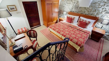 A bedroom with a large bed, a wardrobe, a desk with a telephone, and a chair.