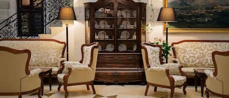 A formal living room with a large wooden cabinet, two sofas, and a staircase with a wrought iron railing.