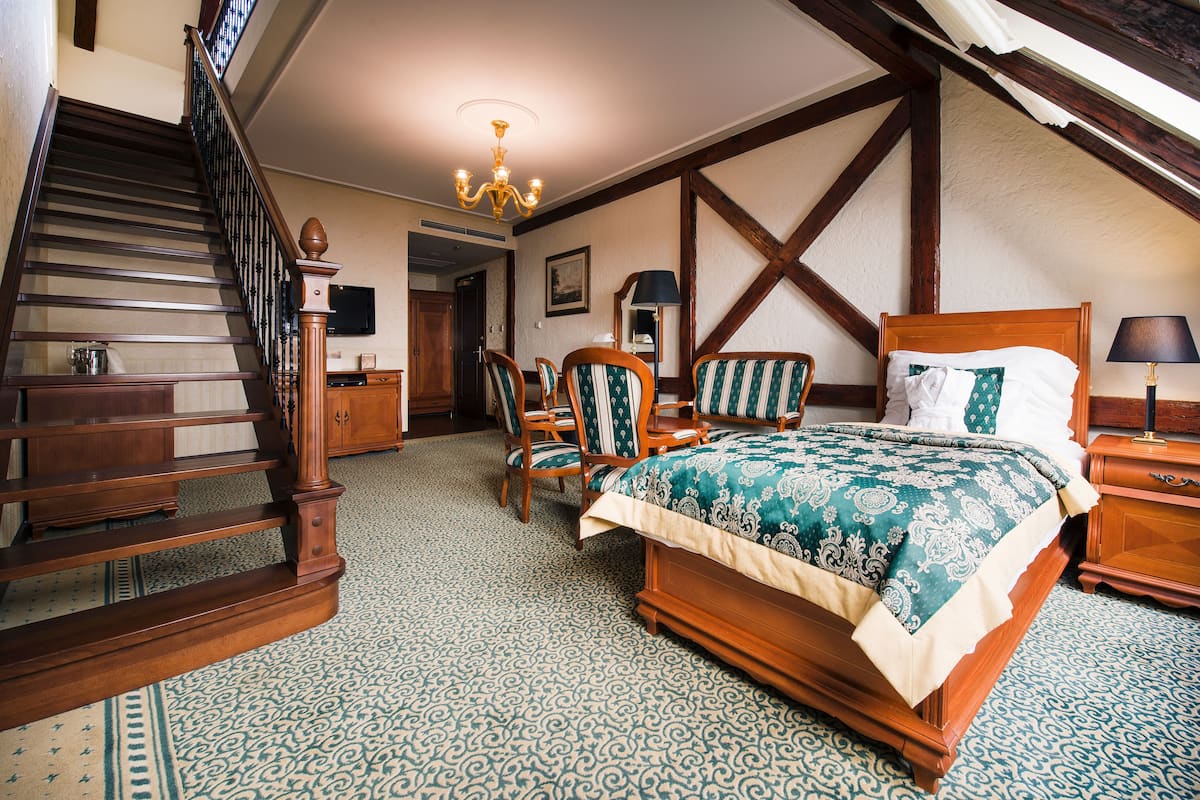Ein Schlafzimmer mit einem hölzernen Bett, einem Sessel, einem Nachttisch, einer Lampe und einer Treppe.