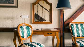 Una habitación con un escritorio de madera, dos sillones tapizados, un espejo y una lámpara de pie.