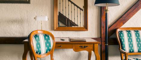 Una habitación con un escritorio de madera, dos sillones tapizados, un espejo y una lámpara de pie.