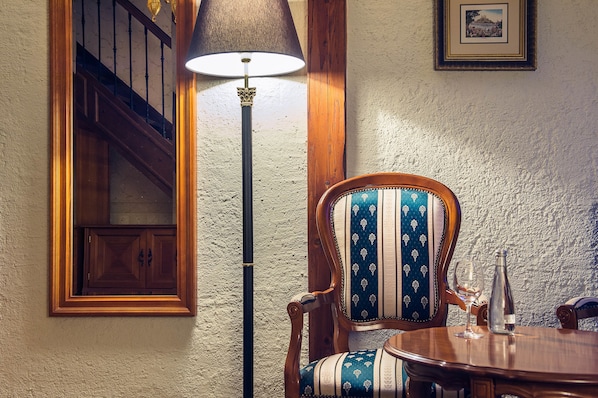 A dining area with a wooden table, a chair with a patterned cushion, a floor lamp, and a framed picture on the wall. - Arcadia Boutique Hotel (Bratislava)