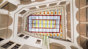 Un atrium con techos altos, una ventana central de vitral, varios tragaluces y una planta colgante.
