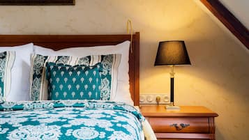 A neatly made bed with patterned bedding, a bedside table with a lamp, and a wooden nightstand.