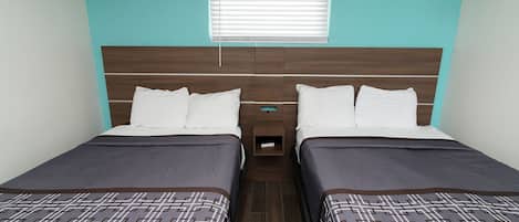 A twin room with two beds, a wooden headboard, a window with blinds, and a small bedside table.