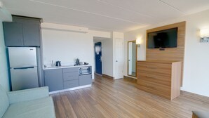 A modern kitchen with grey cabinets, a built-in oven, and a large TV mounted on the wall. - Marjac Suites Virginia Beach Oceanfront (Virginia Beach)