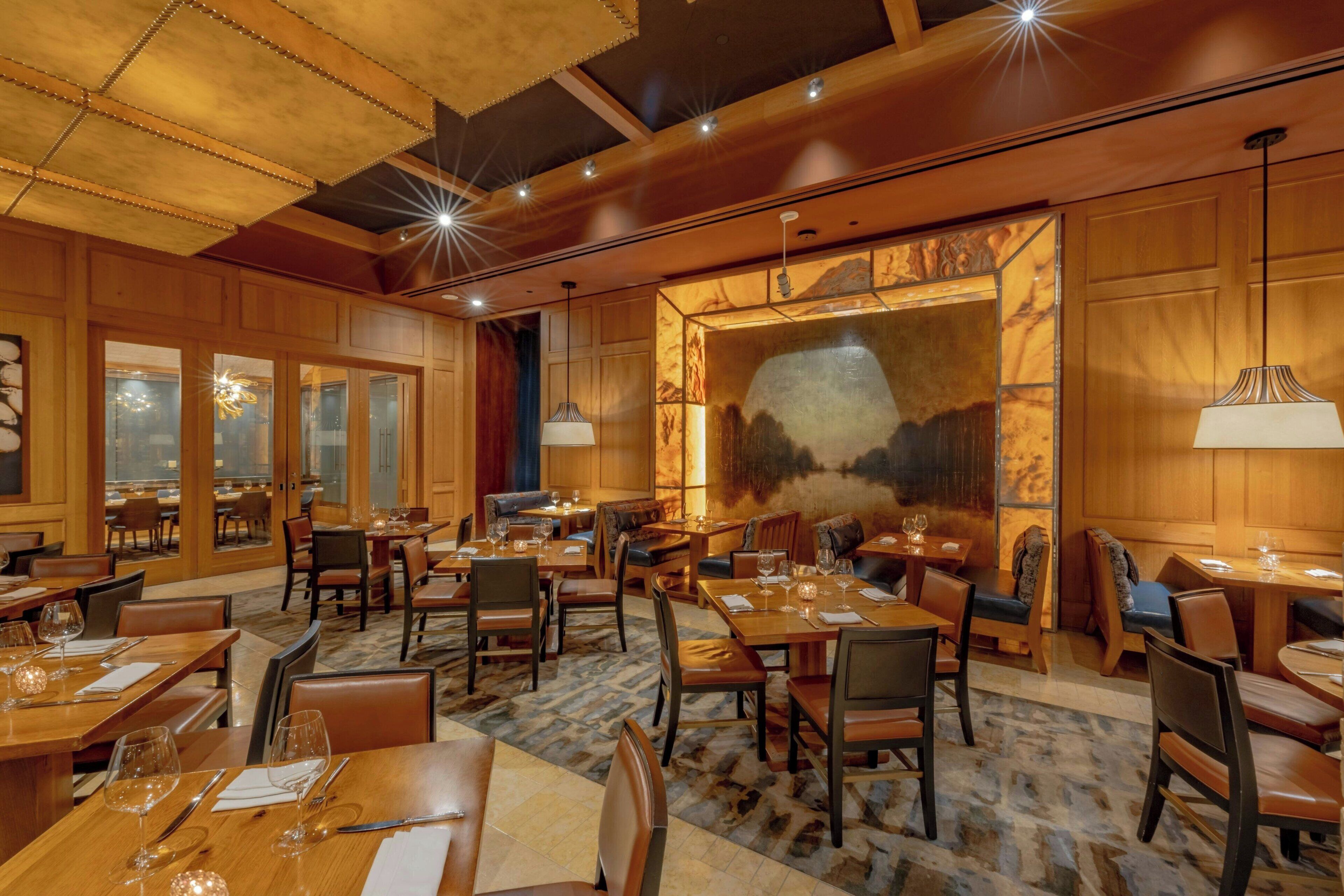 A spacious dining area with multiple tables and chairs, wooden paneling, and large windows.