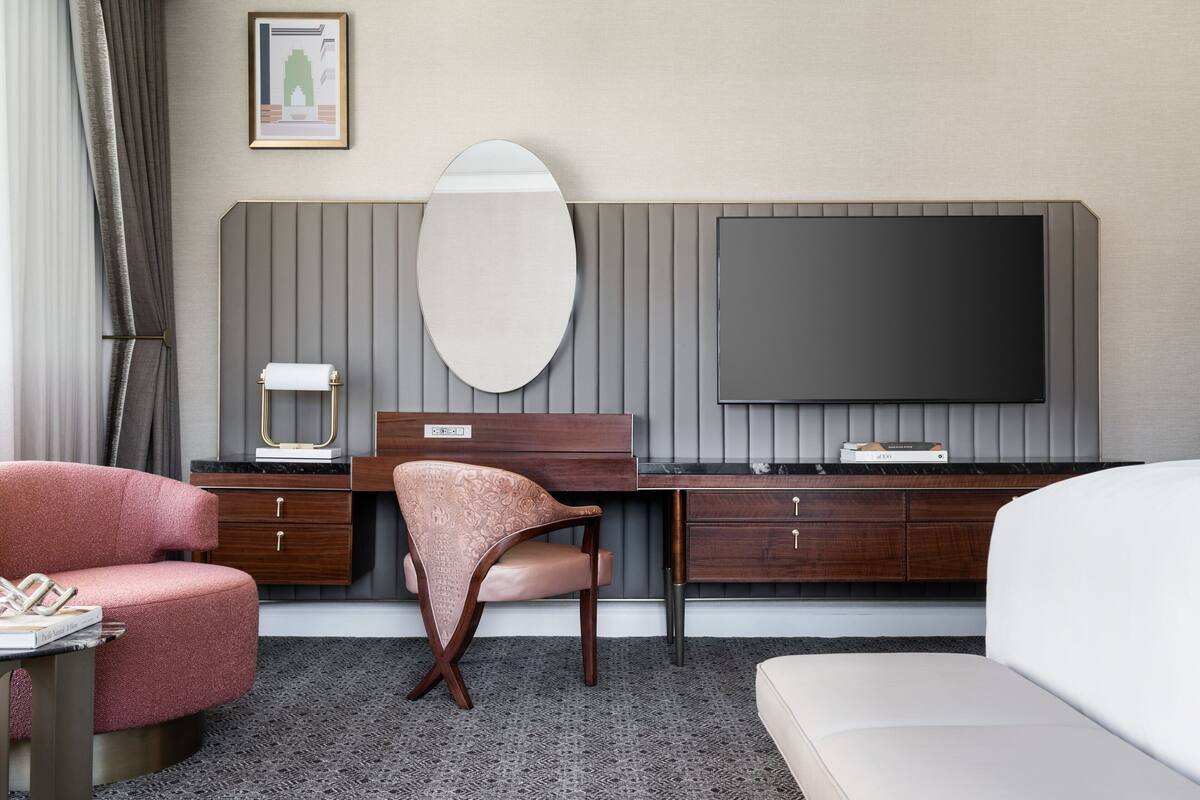 A hotel room with a bed, a desk with a chair, a television, and a large mirror.