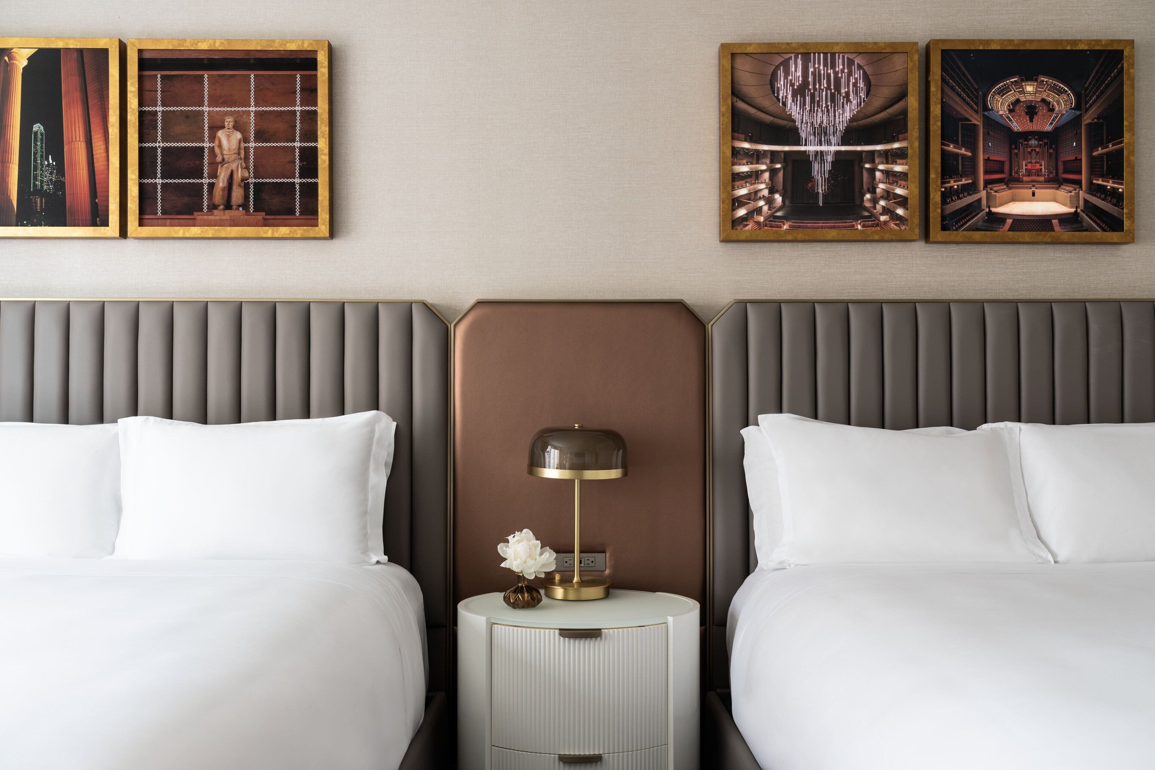A hotel room with two beds, a nightstand with a lamp, and three framed pictures on the wall.