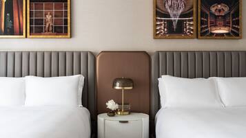 A hotel room with two beds, a nightstand with a lamp, and three framed pictures on the wall.
