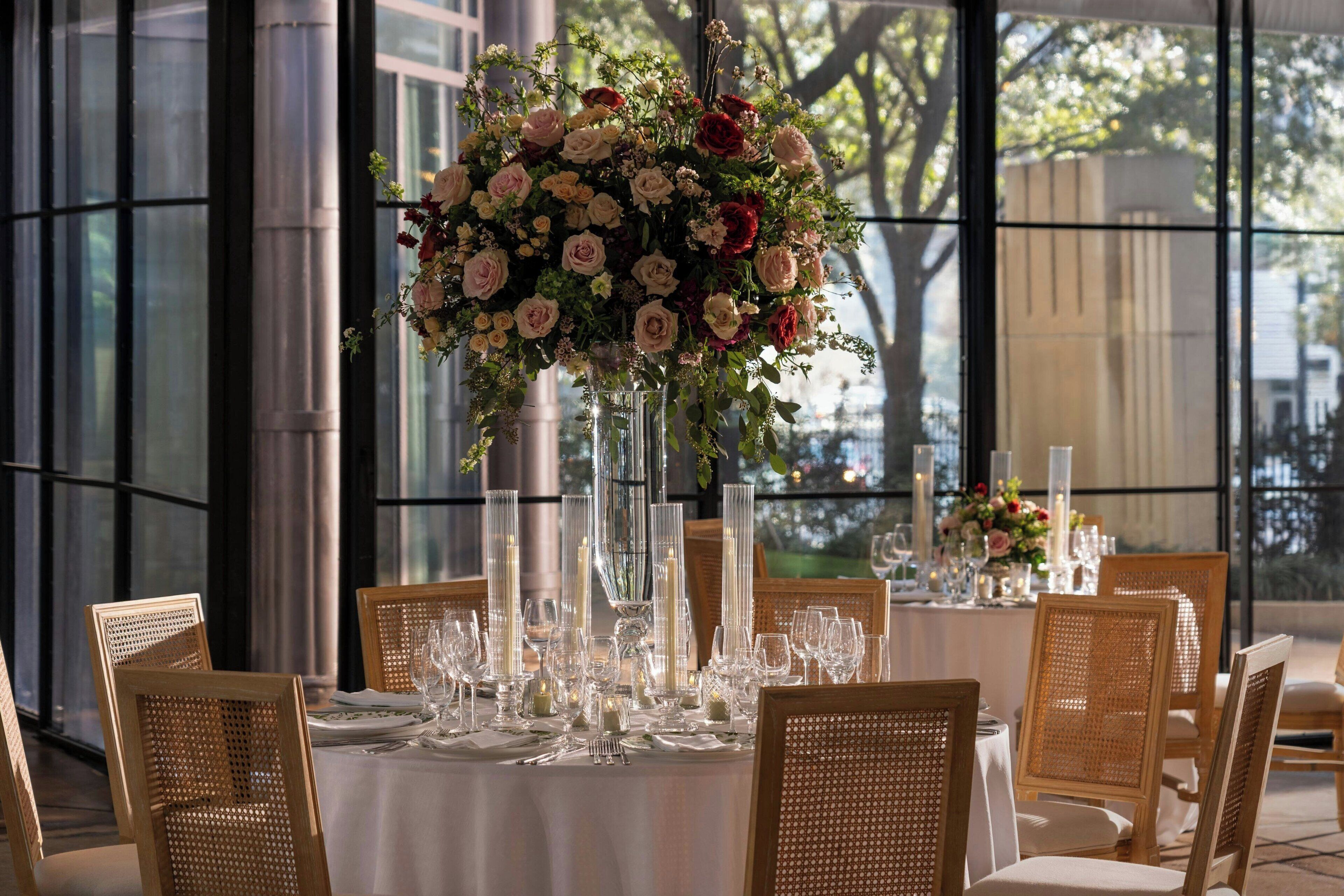 A table set for a formal dinner with a tall floral centerpiece, clear glassware, and wicker chairs.