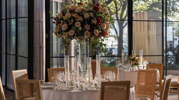 A table set for a formal dinner with a tall floral centerpiece, clear glassware, and wicker chairs.