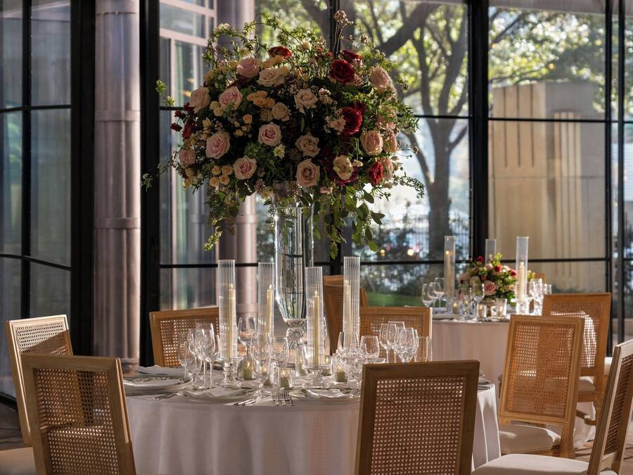 A table set for a formal dinner with a tall floral centerpiece, clear glassware, and wicker chairs.
