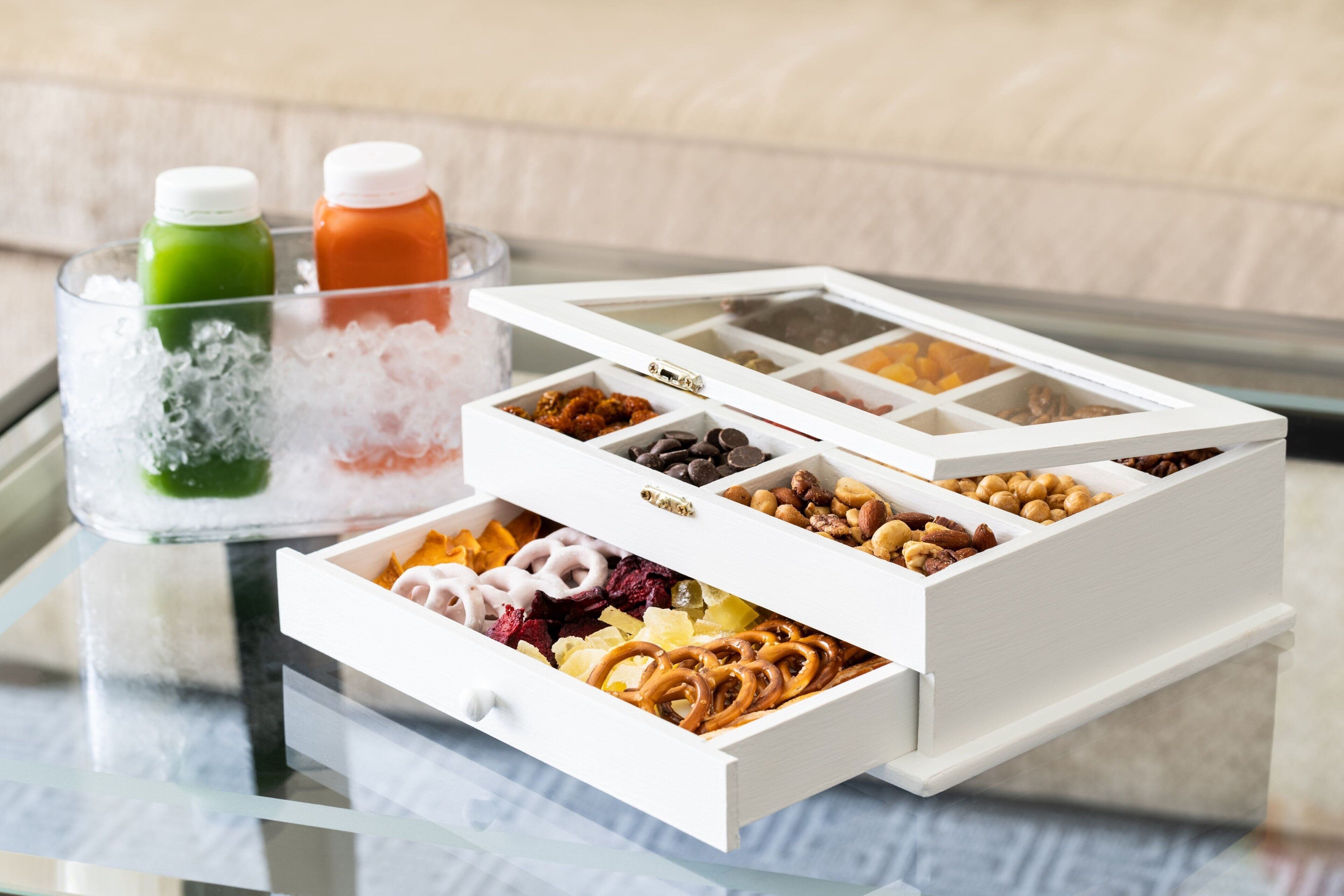 A tray with ice and two bottles, a white box with compartments containing various snacks and dried fruits.