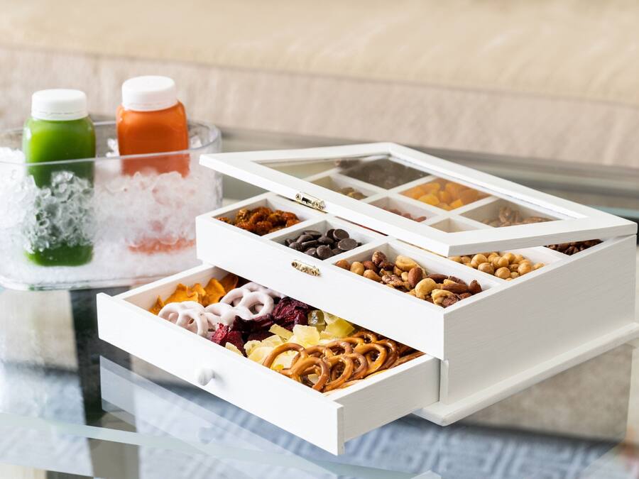 A tray with ice and two bottles, a white box with compartments containing various snacks and dried fruits.