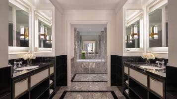 A luxurious bathroom with two large marble sinks, a central bathtub, and a mirror above each sink.